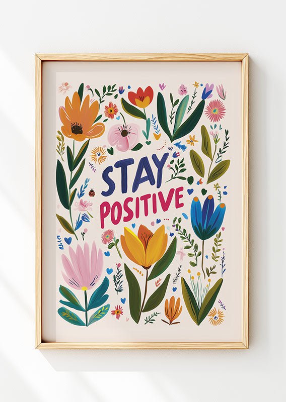 Affiche folk art avec le titre "stay positive" bleu et rose, entourée de fleurs dans un cadre en bois