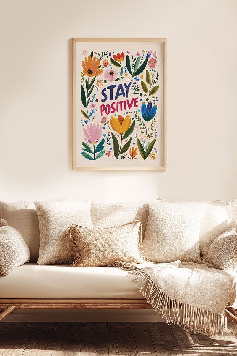 Affiche folk art "stay positive" entourée de fleurs colorées, mise en situation au dessus d'un canapé