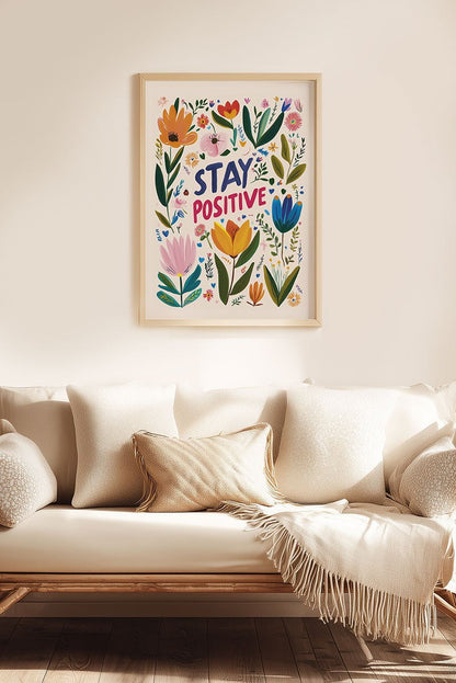 Affiche folk art "stay positive" entourée de fleurs colorées, mise en situation au dessus d'un canapé